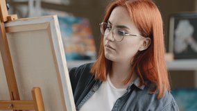 Caucasian woman artist girl painter with red hair put on eyeglasses wearing glasses start art work with oil acrylic paints creates picture drawing painting on canvas inspired student learning draw - Powered by Shutterstock - Get 15% off with code: PIKWIZARD15