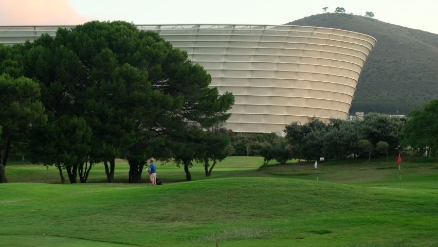 Golfer Hitting Ball with Club on Beatuiful Golf Course. Smiling african american man in cap and sunglasses playing golf. cape town, south africa, stadium, Golfer with golf club taking a shot