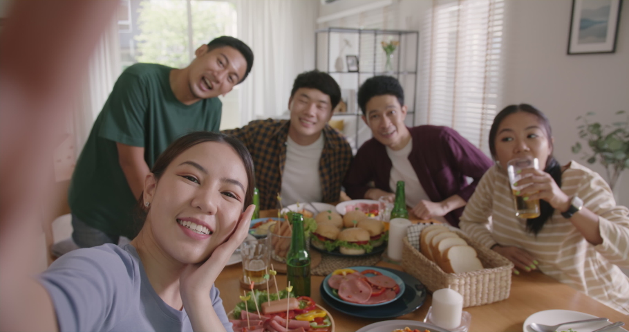 Happy hour diner at home relax smile look at camera shooting video photo on mobile app. Group of asia people young adult friend man and woman sit at dining table joy fun talk or eat food drink beer. Royalty-Free Stock Footage #1092946539