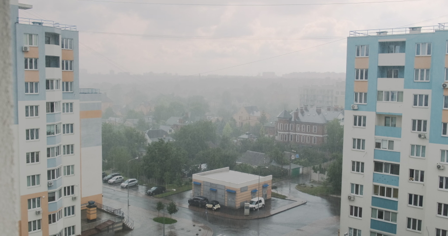 Heavy rain, downpour. View from the window of a multi-storey residential building, urban. Parked cars, cloudy sky.