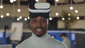 Office male worker using a VR headset, virtual reality concept. Portrait african american software developer standing in office room. It, business and new technologies concept