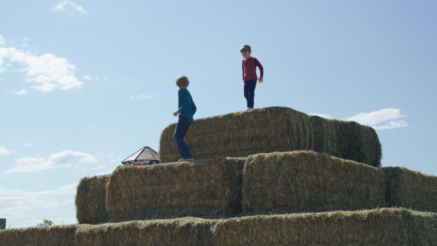 Two boys scale big pyramid pile of hay bales on autumn afternoon