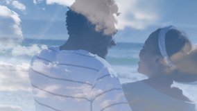Animation of clouds over african american couple at beach. Holiday and digital interface concept digitally generated video.