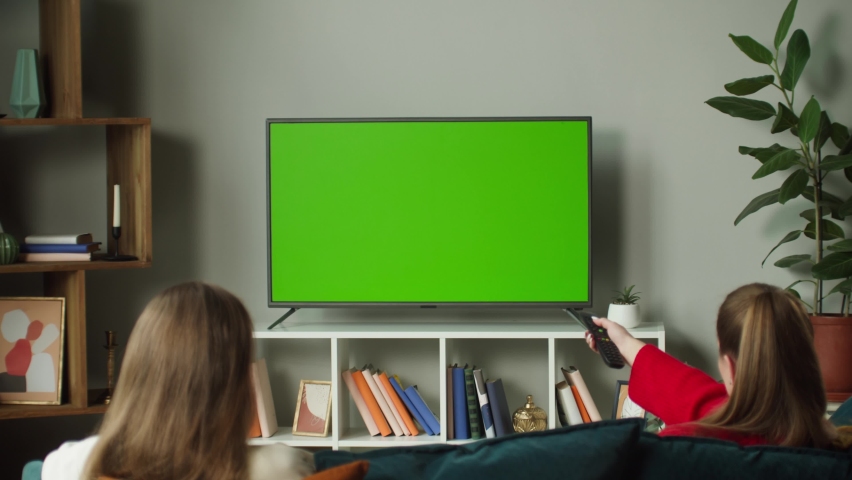 Women watching television with chroma green screen, giving high five. Girlfriends switching channels on tv with remote controller, sitting on sofa in living room. Spare time at home, leisure. | Shutterstock HD Video #1092967559