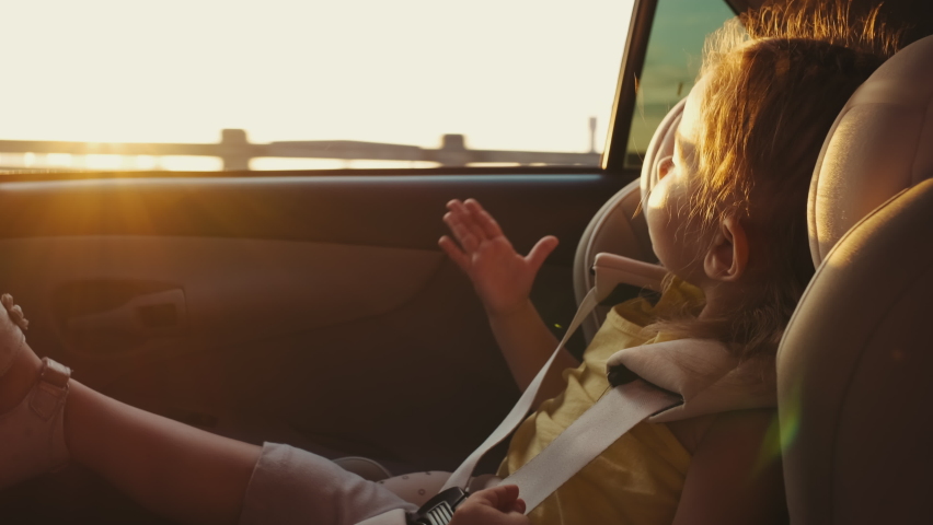 The child sits in a child car seat while the car is moving and looks out the window. Travel concept,Funny life,Summer Time Royalty-Free Stock Footage #1092973125
