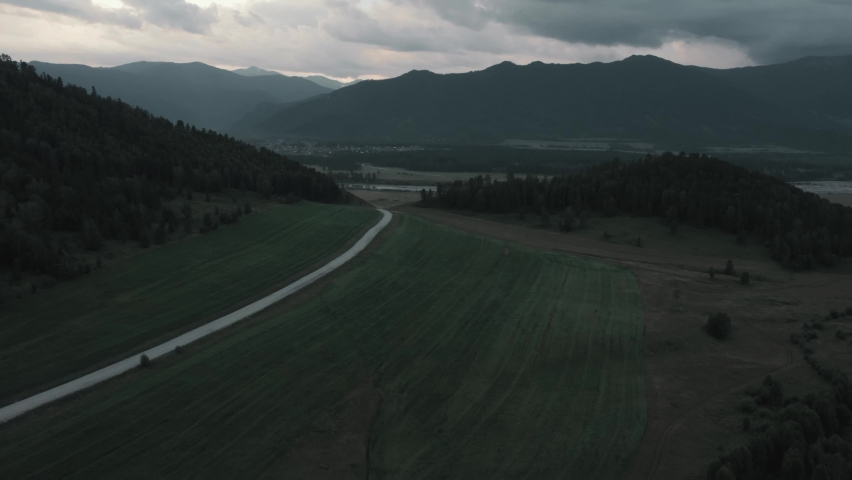 Agriculture and green fields in valley of Altai under dramatic and thunder storm sky, Siberia, Russia. Beautiful summer nature landscape at during sunset. Aerial view from a drone