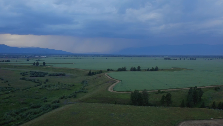 Agriculture and green fields in valley of Altai under dramatic and thunder storm sky, Siberia, Russia. Beautiful summer nature landscape at during sunset. Aerial view from a drone