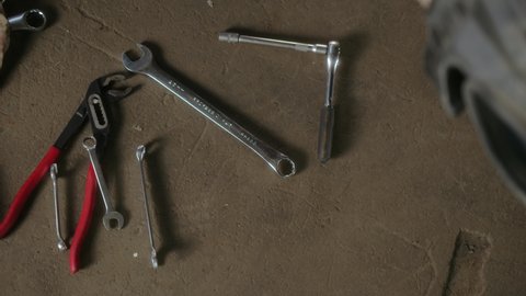 Many different repair tools lie on ground in car service or repair shop. woman hand takes the open-ended key or spanner wrench for work and takes it out of frame.