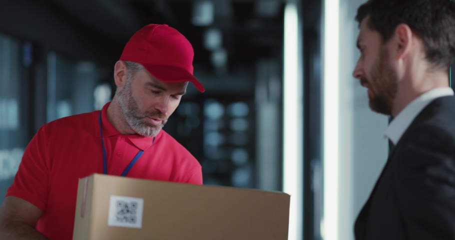 Office executive successful man receiving parcel from fast post delivery services. Customer paying for delivery siging the document.
