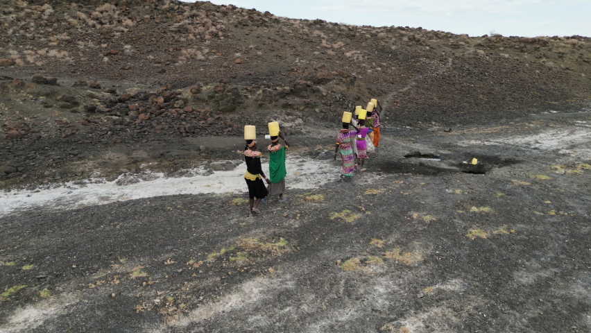 Climate change,drought,water crisis.Aerial view.African woman walking home after collecting water in plastic containers from a volcanic spring, Turkana region, Kenya Royalty-Free Stock Footage #1092979615