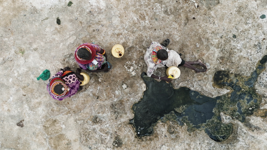Climate change,drought,water crisis.Aerial zoom out view.African woman collecting water in plastic containers from a volcanic spring, Turkana region, Kenya