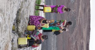 Vertical video. Climate change, drought,  water crisis. Close-up front view. African woman collecting water in plastic containers from a volcanic spring, Turkana region, Kenya