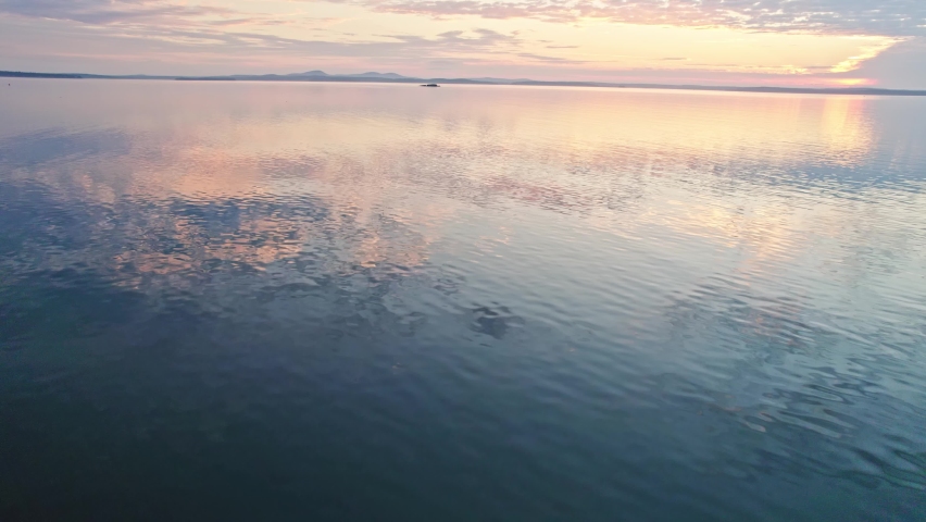Drone shot moving towards sun rising over ocean water horizon 