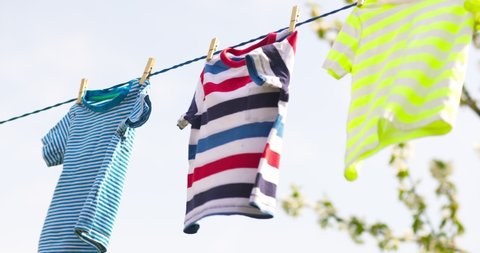 Clean clothes on rope outdoors on laundry day. Colorful t-shirts hanging on a laundry line against blue sky