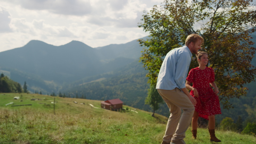 Cheerful family have fun together on summer mountains. Joyful redhair father catching smiling boy on green hill. Happy parents playing with children sunny day outdoors. Carefree holiday on nature.