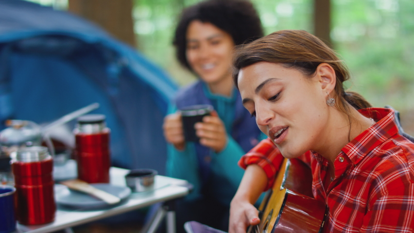 Group of female friends on camping holiday in forest cooking meal and drinking coffee as they sit by tent singing to guitar - shot in slow motion | Shutterstock HD Video #1092987497