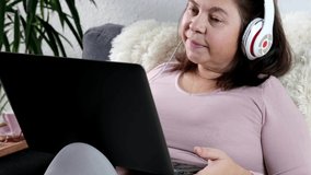 close-up of modern laptop in female hands, middle-aged woman of 50 years old in pink sweater sits on sofa in room, reads news, communicates on Internet, concept of technology, stay at home