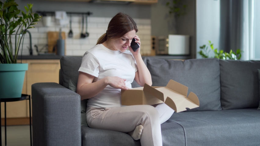 Upset Pregnant woman at home angry and disappointed received the wrong parcel, a female on the couch talking on the phone wrong with shipment delivery, bad service, poor quality product or fraud Royalty-Free Stock Footage #1092994195