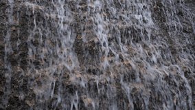 Waterfall close-up. The water flows down the steep stones. Camera movement from bottom to top. Natural abstract background. The concept of movement, calmness, balance. Grey autumn cloudy day