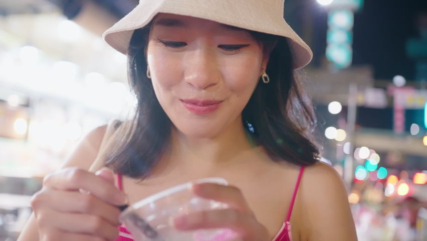 Close up pretty young tourist woman having an asia traditional dessert while walking at China Town. Local Street Food at Night Market. Tourist Attraction and Travel Destination. Life Experiences