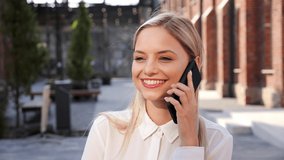 Smiling contented blonde woman talking on mobile phone with friends rejoicing smiling laughing white teeth, outdoors closeup. Girl student makes online order on smartphone outside, satisfied - Powered by Shutterstock - Get 15% off with code: PIKWIZARD15
