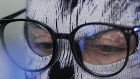 Scam at p2p. Closeup of unknown person in a balaclava and wearing eyeglasses looking at a computer screen with trading charts reflected in glasses. The concept of cybercrime, hacking and security. - Powered by Shutterstock - Get 15% off with code: PIKWIZARD15