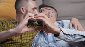 Young gay couple kissing while doing heart symbol with hands at home. High quality 4k footage