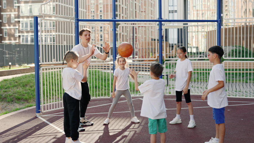 Schoolkids playing with ball on their sport class with male teacher outdoor. Healthy sport and education concept