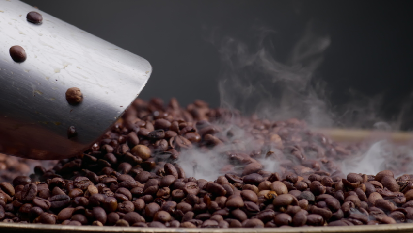 Closeup man hand scooping roasted coffee grains using metal shovel. Light vapor coming over hot aromatic seeds on roaster. Unknown agriculturist preparing coffee beans to grinding for energy drink. Royalty-Free Stock Footage #1093020641