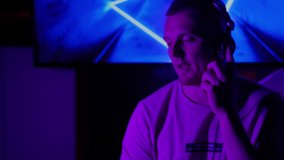 DJ in club using headphones. Male person in earphones change music audio list and mixing sound. Man in purple light dancing and moving. Night relax in nightclub party concept