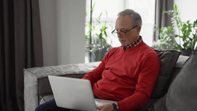 Old man enjoying leisure time while using a laptop on the sofa