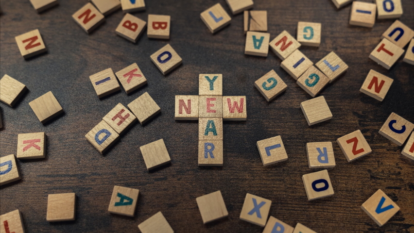 Colourful square letter puzzles creating the words NEW YEAR in the shape of Catholic cross. Dark wooden table as a background. High quality 4k footage