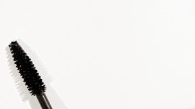 Macro shot and slow motion of a black mascara isolated on white background. Advertising professional cosmetics. Closeup of a mascara wand on white background.