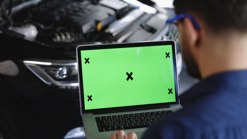 Car Service Mechanic is Running Diagnostics Software on an Advanced Computer with Green Screen Mock Up. Specialist Inspecting the Vehicle in Order to Find Broken Components and Errors in Data Logs. | Shutterstock HD Video #1093044687
