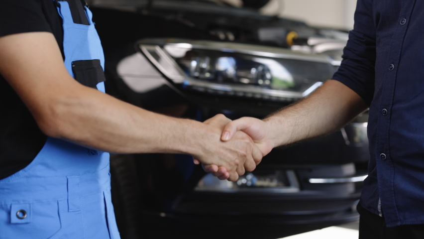 Automotive mechanic repairman handshake with client in garage. Vehicle service manager working in mechanics workshop. Success after check and maintenance car engine for customer. Car repair. Royalty-Free Stock Footage #1093044693