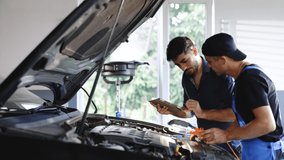 Manager checks tasts on tablet computer and explains an Engine breakdown to an male mechanic. Car service employees inspect car's engine bay with a LED lamp. Modern clean workshop. - Powered by Shutterstock - Get 15% off with code: PIKWIZARD15