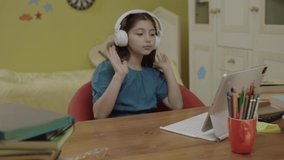 Cute little girl in headphones dancing and singing while sitting with laptop. The little girl who is taking a break from online distance education is dancing to the music she listens to on headphones.
