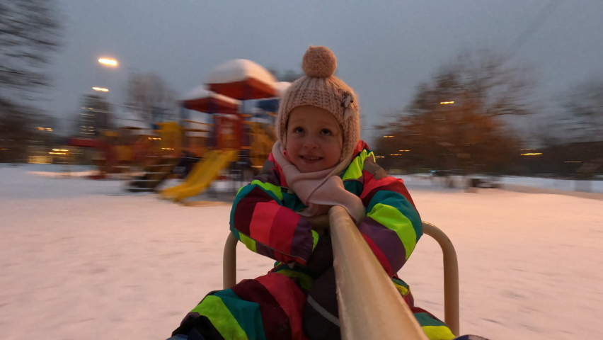 Excited little girl spinning on the merry-go-round, portrait in motion. Happy child having fun on the playground in winter evening Royalty-Free Stock Footage #1093049221