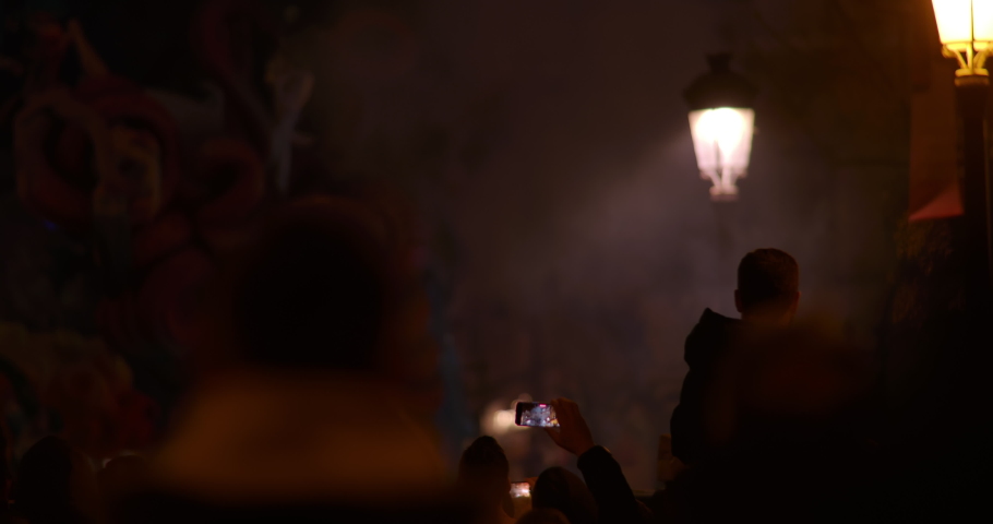 Spain Valencia, taken from the back. Fallas festival, silhouettes of people looking at the bright flashes of fireworks in the night sky, at the figures of Ninot dolls and taking pictures
