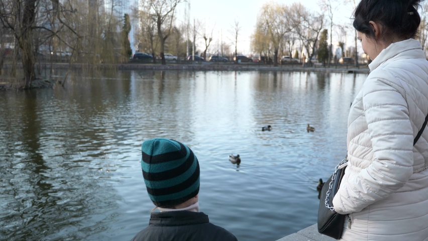 Mother with Child Walk Near Lake Relaxing. Woman and Kid Enjoy Beautiful View on City Cityscape. Spring Sunny Morning. Slow motion 4K