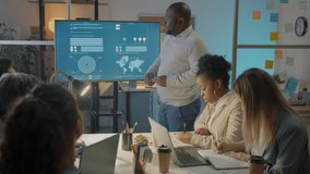 Businessman sharing ideas with creative team talking and pointing at electronic board during presentation in dark office at night. Modern technology and teamwork concept. - Powered by Shutterstock - Get 15% off with code: PIKWIZARD15