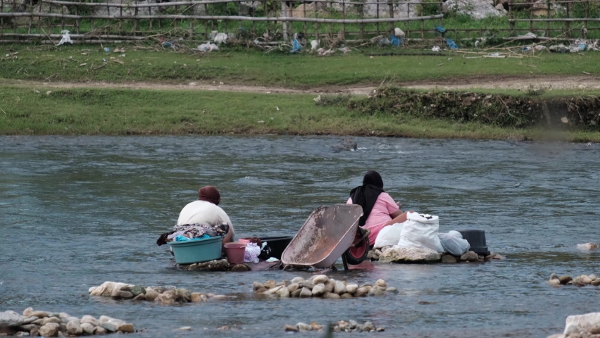Two women are washing clothes beside a river located in Blangpidie, Southwest Aceh Regency in August 2022