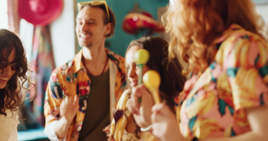 Joyful friends dancing with maracas, having a party in the cafe. Girls and boys, dressed in summer shirts, celebrating an event in the colorful Mexican restaurant Royalty-Free Stock Footage #1093059111