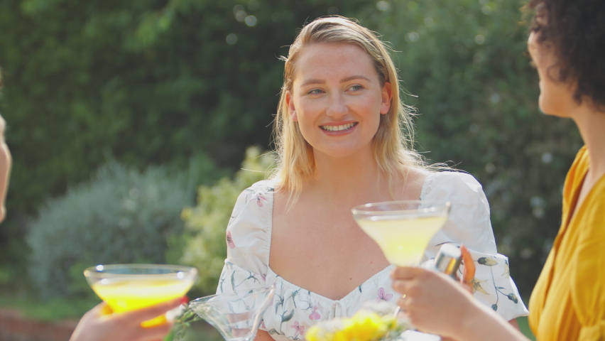 Three female friends sitting outdoors in summer garden at home mixing cocktails - shot in slow motion