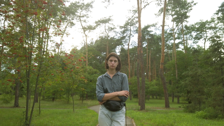 Portrait of young depressed woman standing at the park looking into the camera. Female with sad mood