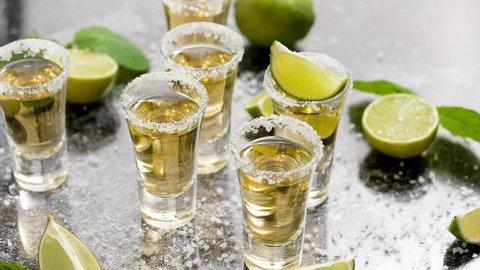 Стоковое видео: Golden Tequila shots served with lime and sea salt on table
