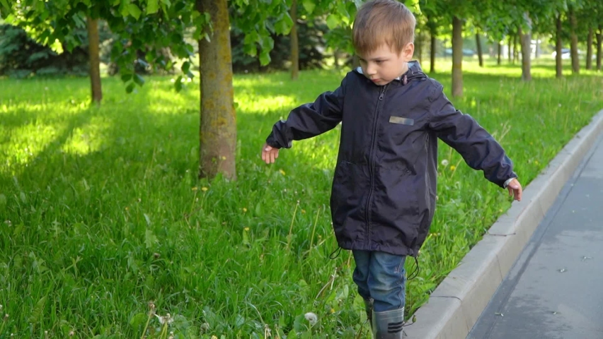 The boy walks along the curb and keeps his balance