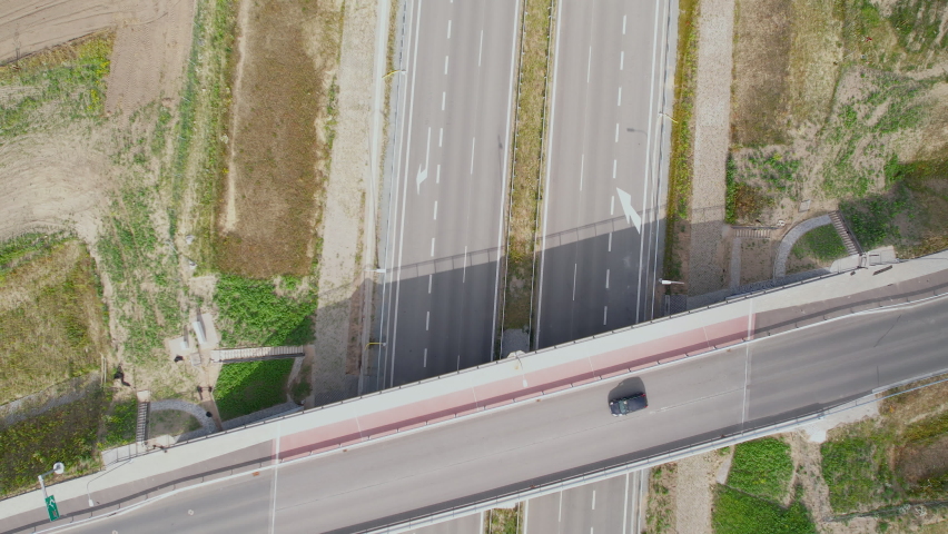 Aerial overhead shot of car crossing bridge road above empty highway at sun