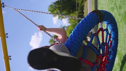 Preschooler caucasian girl swinging on rope net swing on playground 