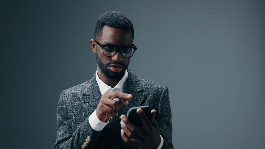 A African American businessman man holding a phone in his hands looks surprised and screams with joy and delight | Shutterstock HD Video #1093081105